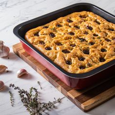 a casserole dish on a wooden cutting board with garlic and herbs around it