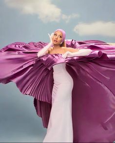 a woman in a long purple dress is holding her arms out and posing for the camera