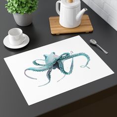 an octopus is sitting on a table next to a cup and saucer with a teapot