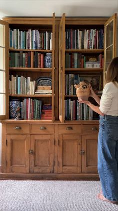 a woman standing in front of a bookcase holding a vase with flowers on it