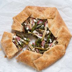 a pizza with asparagus and other toppings cut in half on white paper