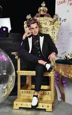 a man sitting on top of a golden chair next to a disco ball wearing a crown