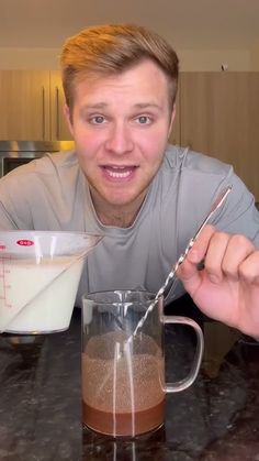 a man holding a spoon in front of a mug with chocolate and milk inside it