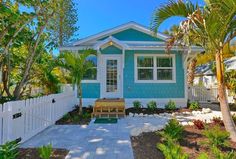 a small blue house with white trim and palm trees in the front yard is shown