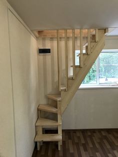 an empty room with wooden stairs and hard wood flooring in the foreground, there is a window on the far wall