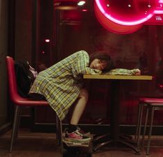 a woman sitting at a table in front of a red neon sign with her head down