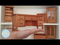 a hand is holding a miniature wooden desk and bookcase in the shape of a doll house