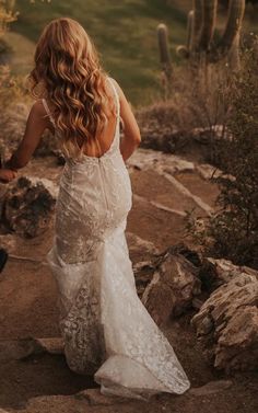 a woman in a wedding dress walking down a dirt path with her back to the camera