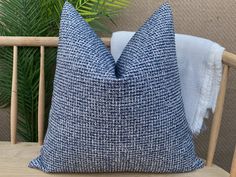 a blue and white pillow sitting on top of a wooden chair next to a plant