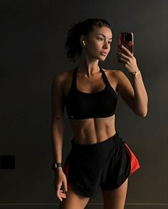 a woman taking a selfie with her cell phone while wearing black sports bra and shorts