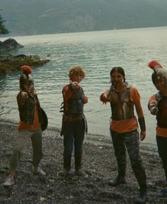 four people standing on the shore of a body of water wearing life vests and helmets