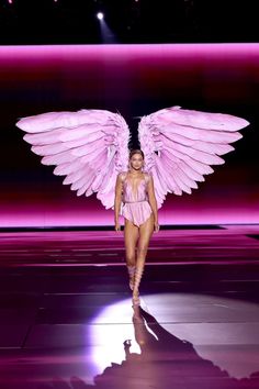 a model walks down the runway with large pink wings