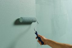 a person holding a paint roller in their hand and painting the wall with blue color