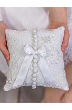 a person holding a white pillow with a bow on the front and back of it