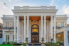 a large white house with pillars and columns on the front door, surrounded by greenery