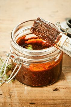 a jar filled with some kind of sauce on top of a wooden table next to a brush