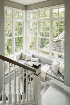 a window seat with pillows on it next to a stair case in front of two windows