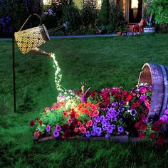 a garden with flowers in the grass and a watering can filled with lights on it