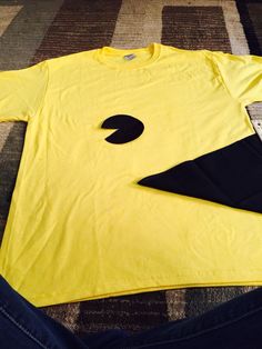 a yellow t - shirt with a black bird on it sitting on the floor next to a pair of jeans