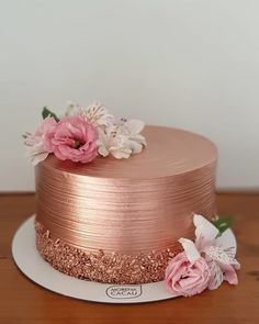 there is a pink cake with flowers on the top and gold frosting around it