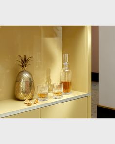 two vases and three glasses sitting on a counter in front of a yellow wall