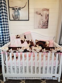 a baby crib in a room with pictures on the wall and cow print bedding