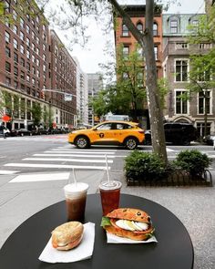 a table with food and drinks on it in front of a yellow taxi parked at an intersection