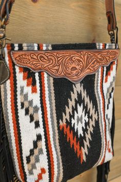 Glendive Wool Tooled Leather Crossbody Bag Glendive is a beautiful uniquely designed bag for any occasion! This tooled leather crossbody features black and brown Aztec wool body adorned with tooled leather accent, removable tooled leather shoulder strap, black fringe, zippered top closure, cotton liner, interior zipper pocket, and 2 interior slip pockets. Add western flair to any outfit with this beauty! Product Details Black Brown Aztec Wool Body Tooled Leather Accent Removable Tooled Leather S Black Hand Tooled Tote Shoulder Bag, Black Hand Tooled Tote Bag, Artisan Black Crossbody Shoulder Bag, Artisan Black Crossbody Bag, Black Hand Tooled Artisan Bag, Black Artisan Hand-tooled Bag, Artisan Hand Tooled Black Bag, Artisan Hand-tooled Black Bag, Artisan Black Hand-tooled Bag