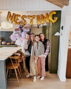 three women standing in front of a table with balloons and letters hanging from the ceiling