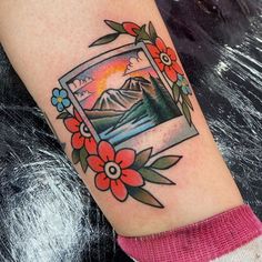 a woman's arm with a tattoo on it that has flowers and mountains in the background