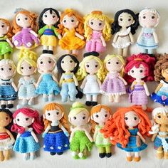 there are many small knitted dolls lined up on the white tablecloth, each with different outfits and hair colors