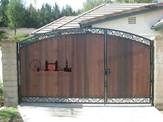 an iron and wood driveway gate in front of a house with two cats on it