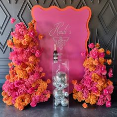 a bottle of alcohol sitting next to some pink and orange flowers in front of a sign