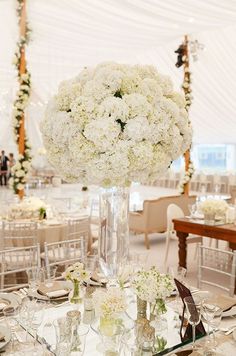 a tall vase filled with white flowers sitting on top of a table covered in silverware