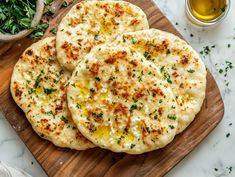 three pita breads on a cutting board next to some parsley and garlic