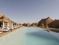 an empty swimming pool with lounge chairs and umbrellas in front of the mountainside