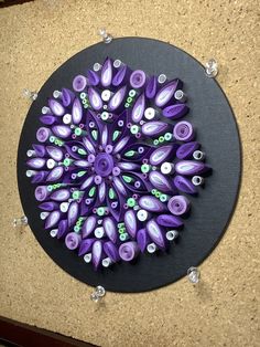 a purple and green circular artwork on a black plate with white dots in the center