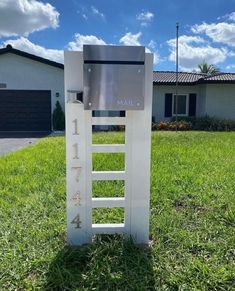 a white sign sitting in the middle of a grass covered field next to a house