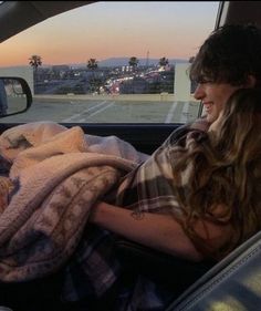 a woman sitting in the back seat of a car holding a blanket and looking out the window