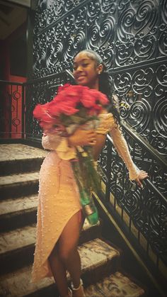 a woman in a dress is holding flowers on the stairs with wrought iron railings behind her