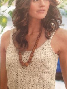 a woman with long brown hair wearing a white tank top and wooden beaded necklace