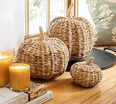 three wicker pumpkins sitting on a table next to some books and candles in front of a window