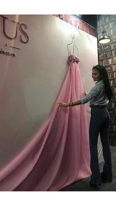 a woman standing next to a pink dress on display in front of a bookcase