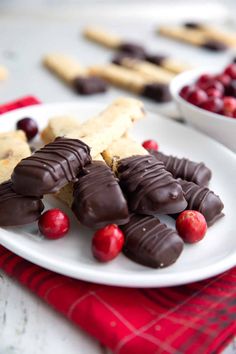 a white plate topped with chocolate covered cranberries and crackers next to bowls of cookies