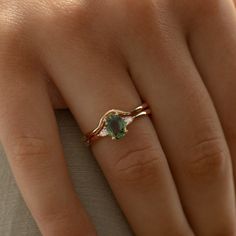 a woman's hand with a gold ring and green stone on top of it