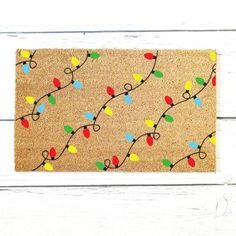 a door mat decorated with christmas lights on white wood planks and painted in bright colors