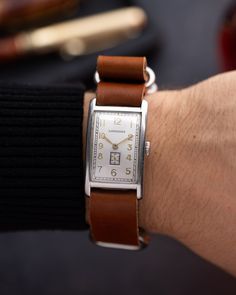 This vintage Longines timepiece embodies the elegance of the Art Deco era with its sleek 25 mm x 36 mm rectangular case, showcasing clean lines and timeless design. The silver dial is adorned with bold gold-tone Arabic numerals and minimalist golden hands, a hallmark of the Art Deco aesthetic. The subdial for seconds at 6 o'clock adds both functionality and a touch of geometric precision, typical of the era's style.  The watch's Art Deco case is complemented by a brown leather strap, which bring Classic Rectangular Watches With Date Display, Timeless Rectangular Chronometer Watch, Timeless Rectangular Watch, Vintage Rectangular Chronometer Watch, Vintage Silver Business Watch, Vintage Silver Watches For Business, Silver Vintage Business Watches, Vintage Jewelry And Watches With Diamond Hour Markers, Timeless Watch Accessories With Date Display As Gift