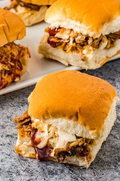 two pulled pork sandwiches on a plate with another sandwich in the background and one cut in half