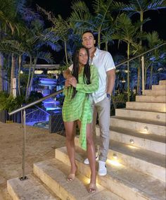 a man and woman are standing on the stairs in front of palm trees at night