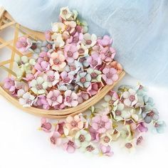 small pink and white flowers sitting in a wooden basket next to a blue cloth on the floor